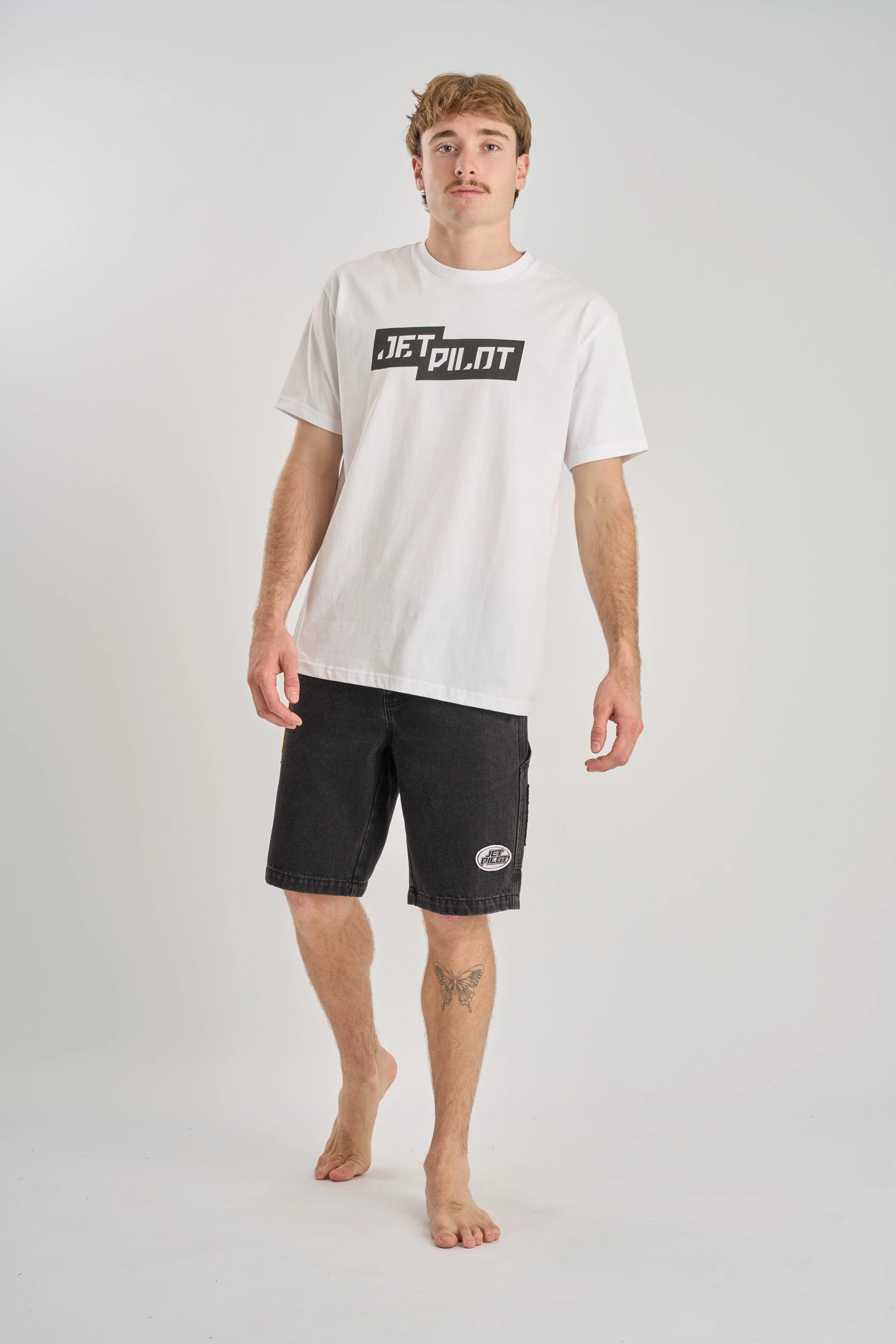 Man wearing a white t-shirt with 'Jetpilot' logo and black shorts on a white background