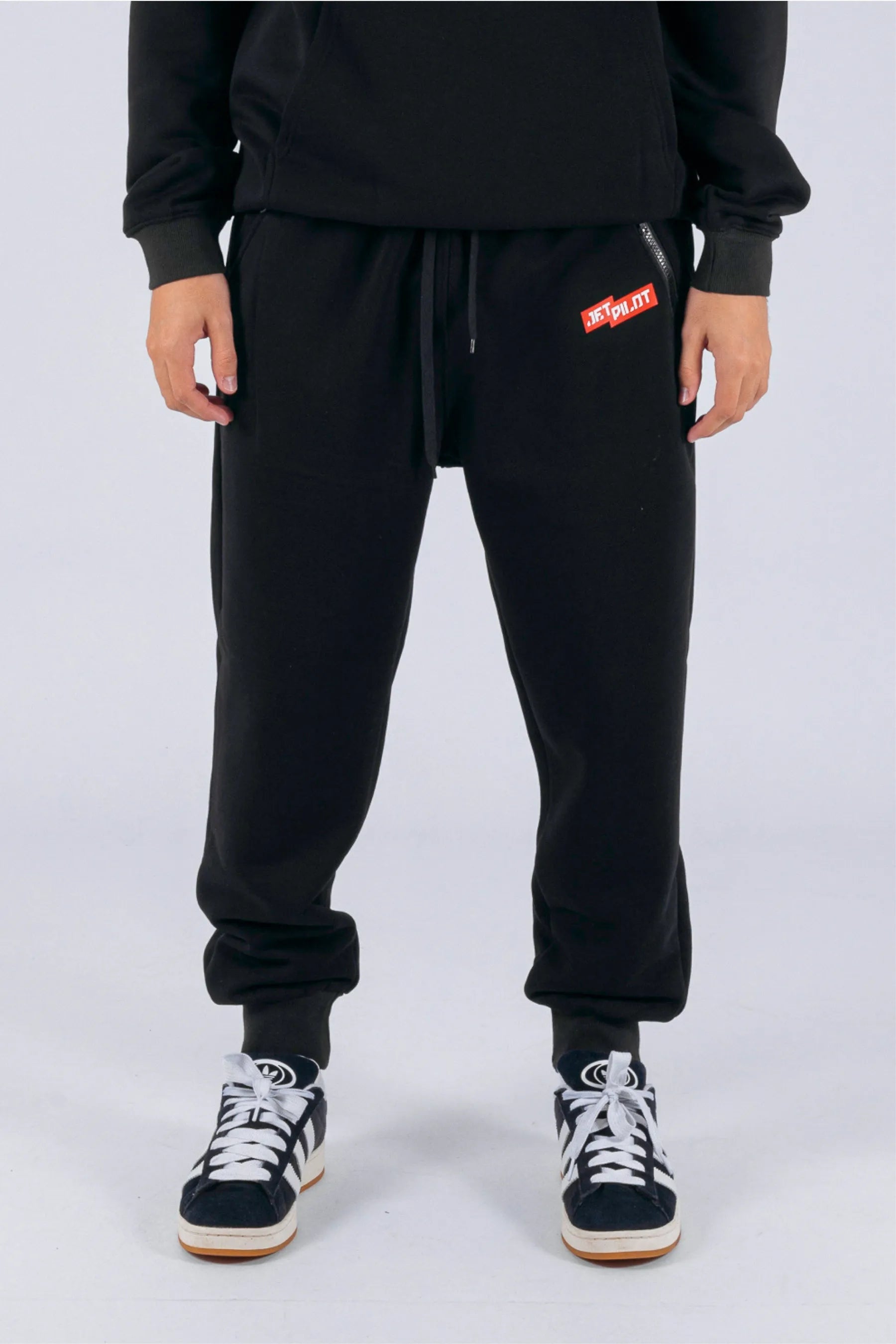 Front view of a person wearing black trackpants with a red Jetpilot logo on a white background — view 1 (3)