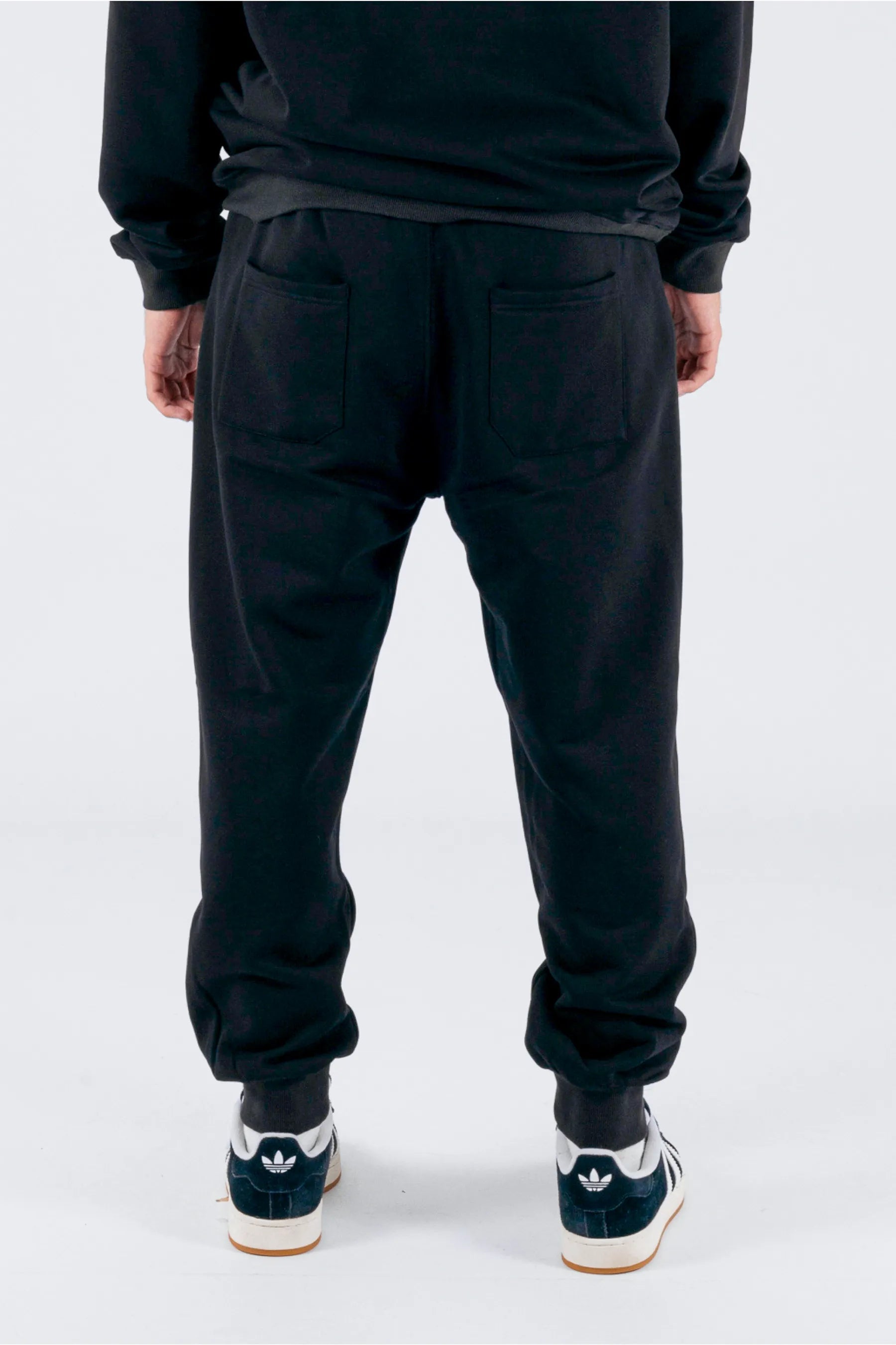 Back view of a person wearing black trackpants on a white background — view 2 (3)