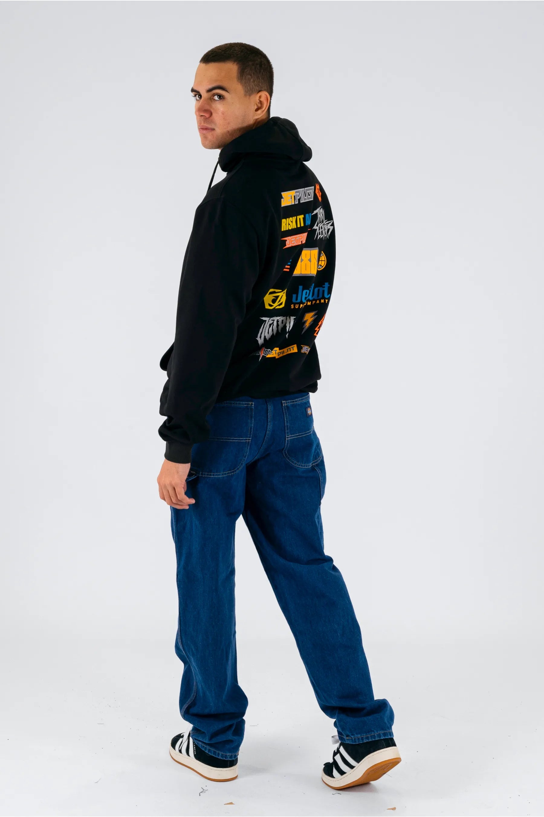 a person wearing a black pullover with a Jetpilot logos, blue jeans and a black/white shoes — view 3 (3)