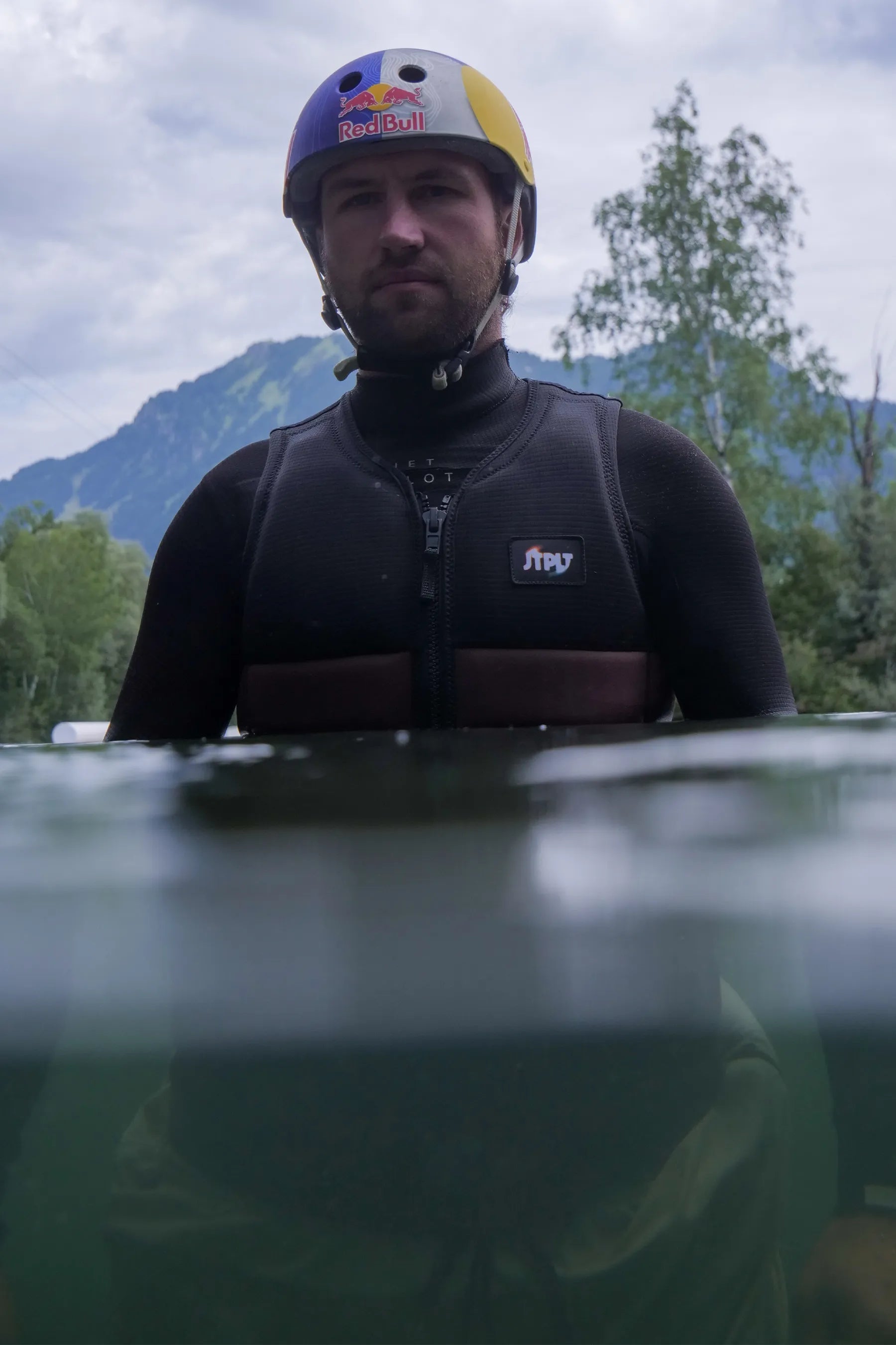 Person wearing a Jetpilot X1 Life Jacket - Felix Georgii Signature Series - Black/Brown, in water and helmet with a mountainous background