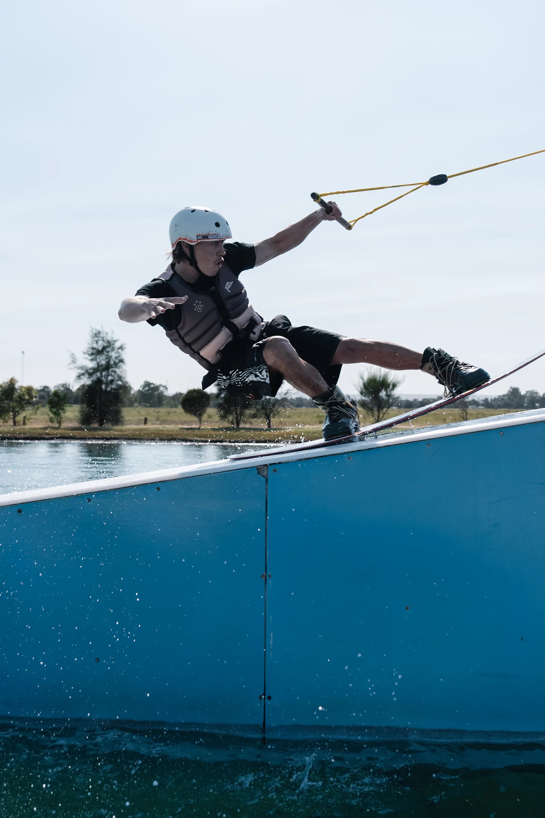 Person wakeboarding on a blue ramp with trees and clear sky in the background wearing a Jetpilot X1 Life Jacket - JTPLT X Heatley - Brown