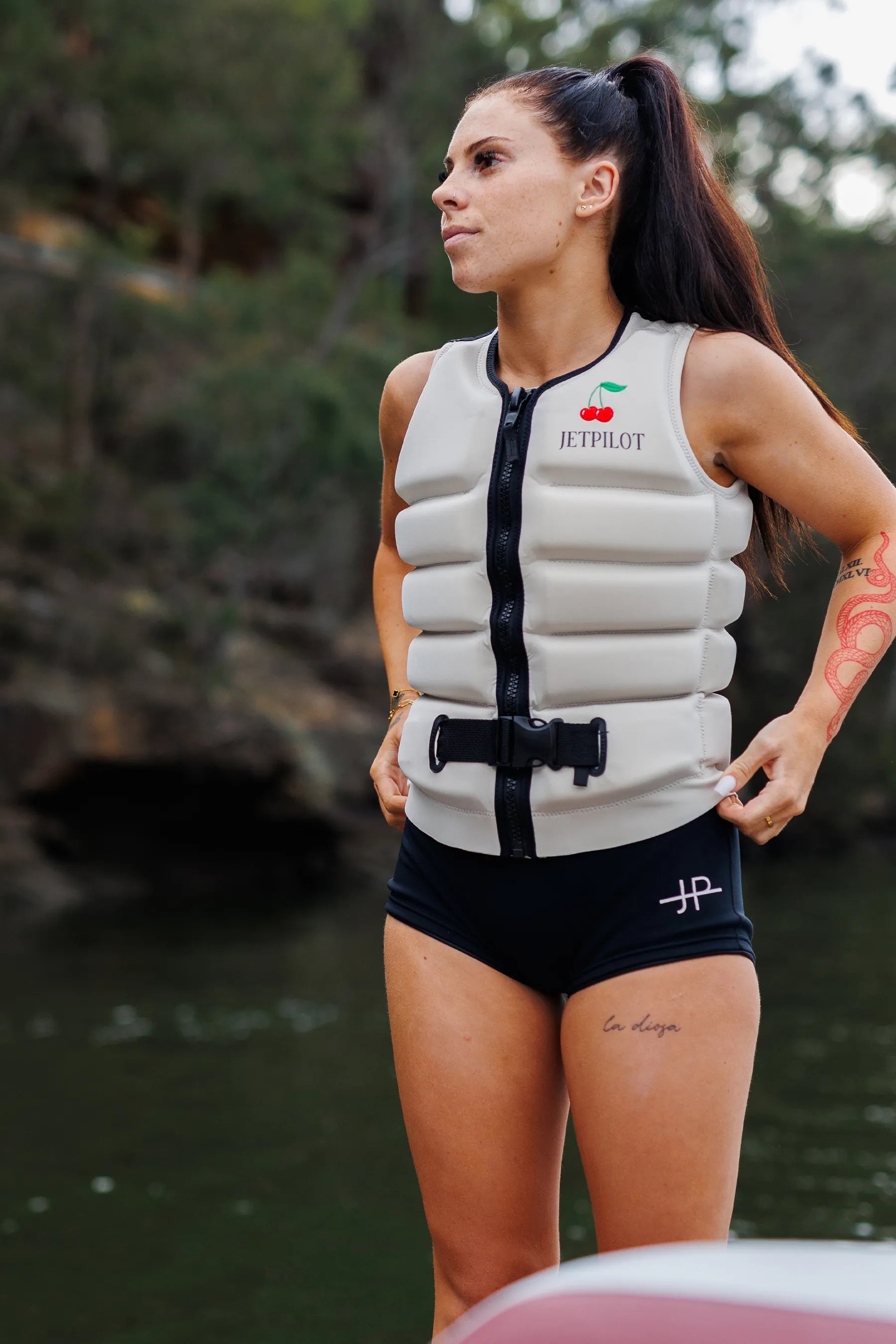 Wakeboarder in Jetpilot X1 Ladies Life Jacket - Zahra Kell Signature Series - Off White, standing at the back of the boat, on a body of water.