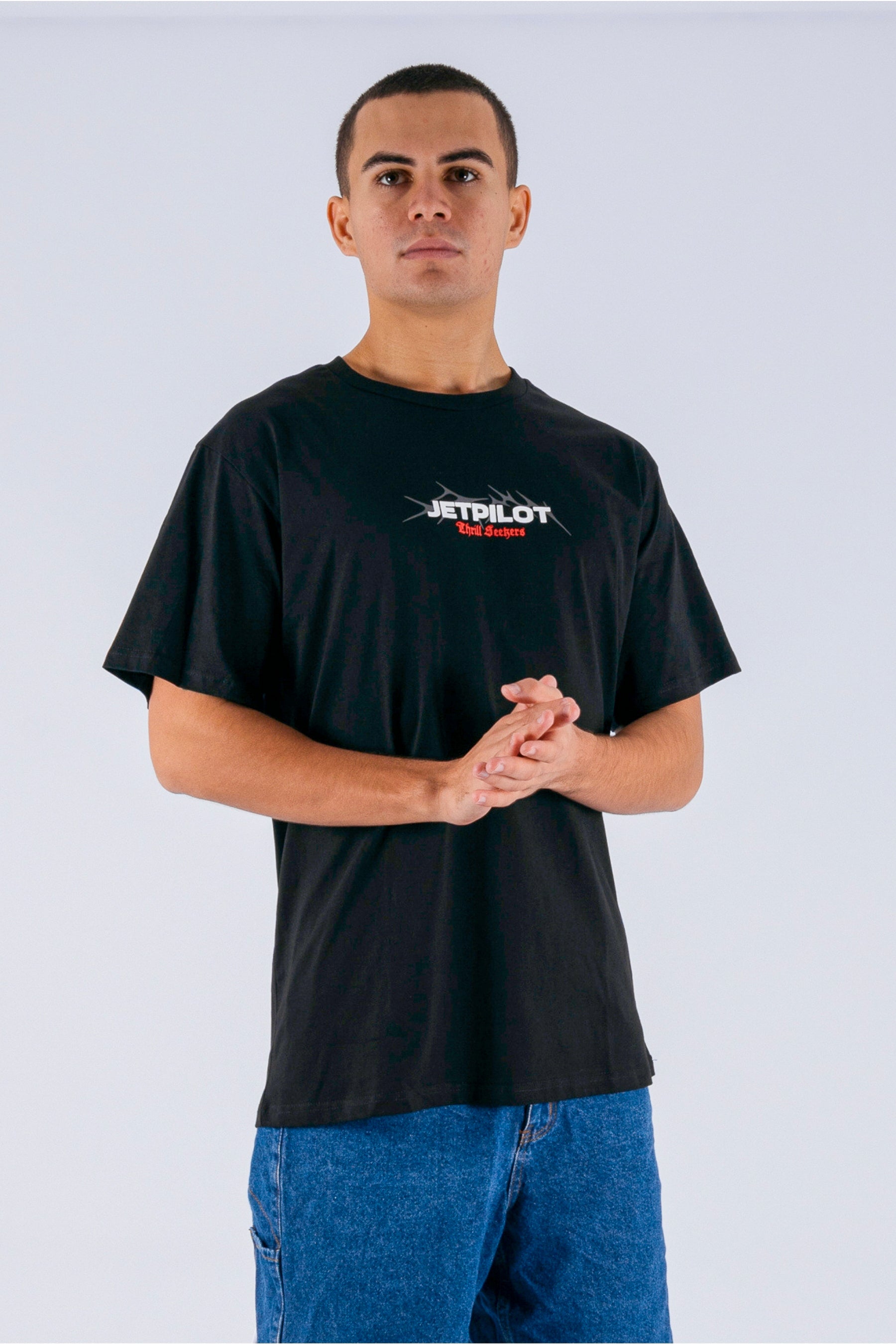 A person holding his hands together, wearing a black tee with a white Jetpilot logo on a white background — view 4 (3)