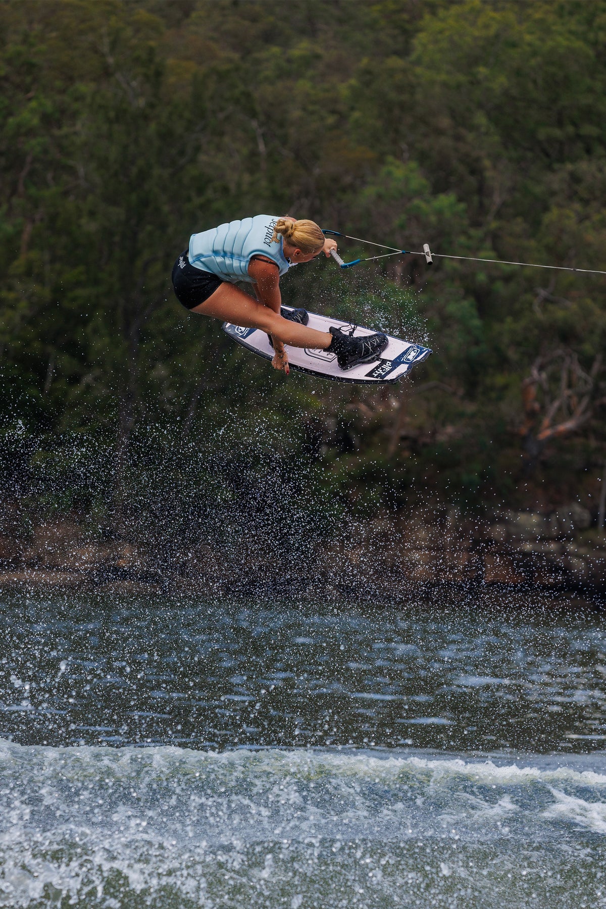 Rider in the air over the wake on a wakeboard, wearing the Ice Blue Zahra X1 life jacket